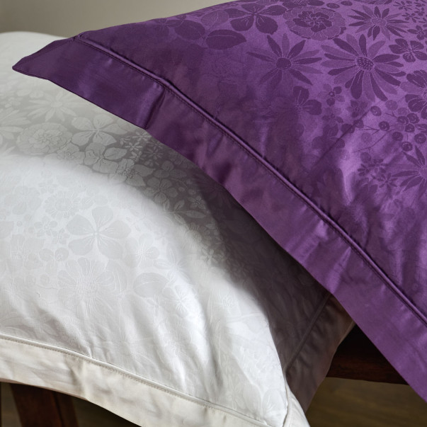 Détail du motif floral jacquard de la taie d’oreiller Magnolia en coloris violet, avec finition passepoilée.