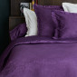Linge de lit Magnolia en coloris violet, avec taie de traversin unie et taies d’oreiller jacquard assorties.